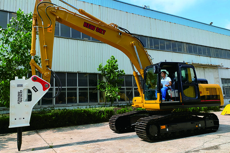 Yellow NEW SKY excavator equipped with a white GBPSC hydraulic breaker (hammer), parked in front of a factory with an operator in the cab. Yellow NEW SKY excavator equipped with a white GBPSC hydraulic breaker (hammer), parked in front of a factory with an operator in the cab.